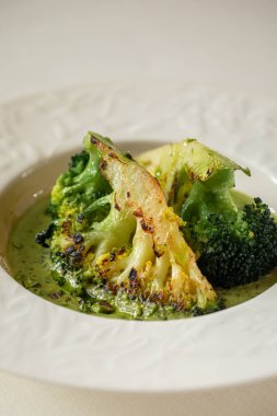 Kızarmış brokoli çiçekleri, restoran ortamında beyaz tabakta bol kremalı yeşil sosla servis edilir.