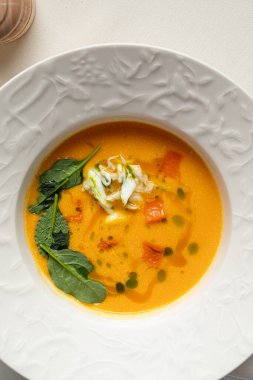 Sütlü sebze çorbası, taze otlar ve krema, beyaz kasede servis ediliyor.