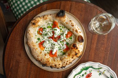 İtalyan usulü üzerine füme somon peyniri ve ahşap masada servis edilen taze soğanlı pizza.