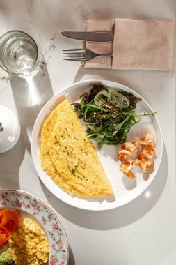 Tüylü omlet, ızgara karides ve taze yeşil salata ile servis edilir. Parlak restoran ortamında beyaz tabakta.