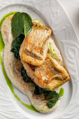 Tavada kurutulmuş beyaz balık krem soslu ıspanak ve bitkisel yağla servis edilir.