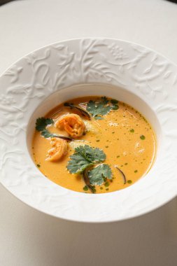Karides otlu kremalı deniz ürünleri çorbası ve beyaz seramik tabakta servis edilen zengin dokular.