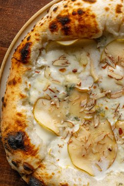 İtalyan usulü pizza dilimlenmiş armut gorgonzola peyniri ve ahşap masada servis edilen kremalı beyaz sos.