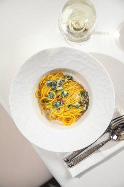 Beyaz kasede servis edilen kremalı ıspanak makarnası. Restoran masasında bol soslu.