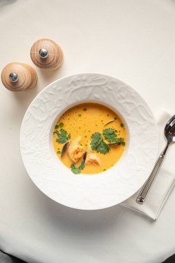 Karides otlu kremalı deniz ürünleri çorbası ve beyaz seramik tabakta servis edilen zengin dokular.