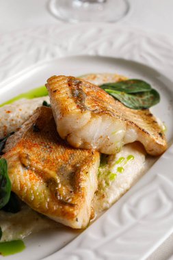 Tavada kurutulmuş beyaz balık krem soslu ıspanak ve bitkisel yağla servis edilir.