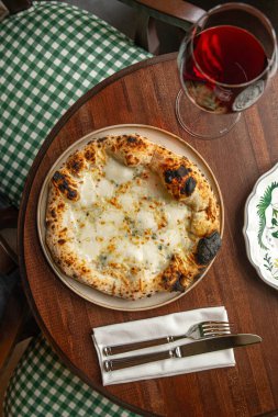 İtalyan dört peynirli pizza, ahşap masada servis ediliyor. Sıcak bir restoranda bir bardak kırmızı şarapla servis ediliyor.