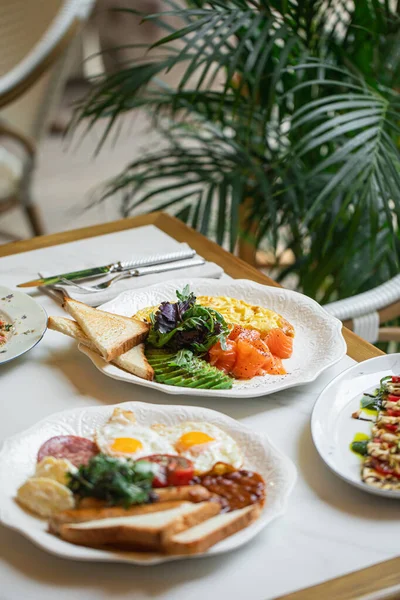 Lokanta masasında gün ışığıyla servis edilen omlet somonlu avokado tostlu nefis kahvaltı tabağı.