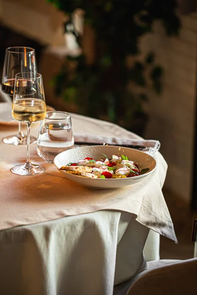 Taze salata, dilimlenmiş balık, şifalı otlar ve ılık bir beyaz şarapla nefis bir restoran masası.