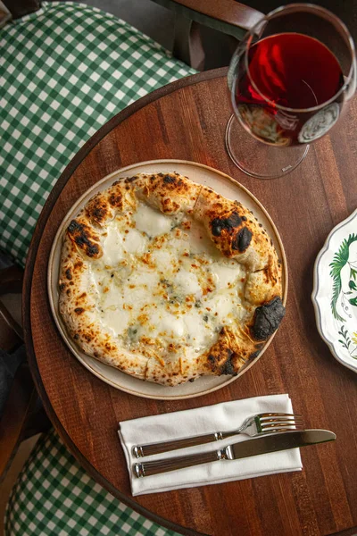 İtalyan dört peynirli pizza, ahşap masada servis ediliyor. Sıcak bir restoranda bir bardak kırmızı şarapla servis ediliyor.