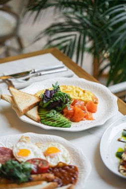 Lokanta masasında gün ışığıyla servis edilen omlet somonlu avokado tostlu nefis kahvaltı tabağı.