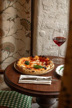 Eritilmiş mozzarella soslu klasik margherita pizza ve bir bardak kırmızı şarapla servis edilen taze fesleğen.