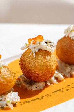 Kırmızı havyarla kaplanmış altın kızartılmış yengeç kroketleri zarif restoran tarzında kremalı portakal sosuyla servis ediliyor.