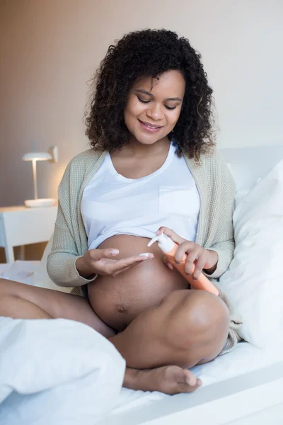 Беременная женщина увлажняет живот — стоковое фото