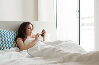 Yatakta akıllı telefonlu bir kadın