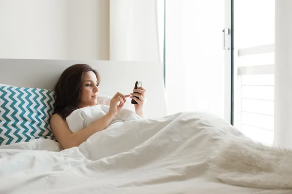 Mulher na cama com smartphone — Fotografia de Stock