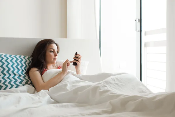 Γυναίκα στο κρεβάτι με smartphone — Φωτογραφία Αρχείου