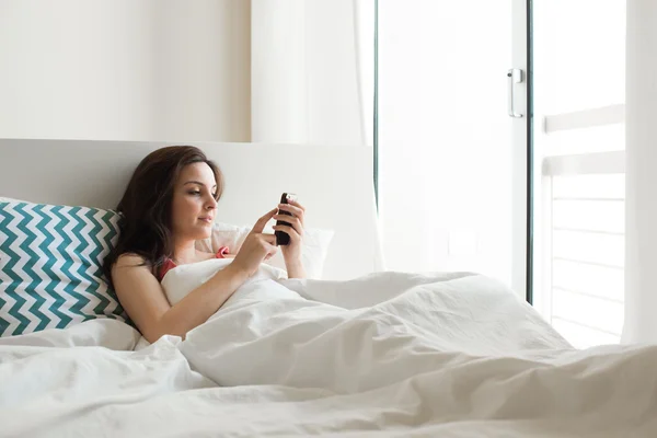 Vrouw in bed met smartphone — Stockfoto