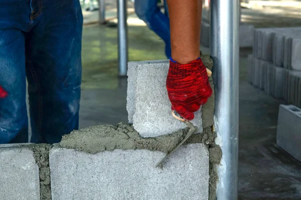 Plaster worker wearing red gloves is laying bricks.