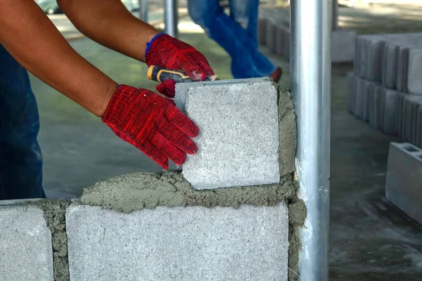 Plaster worker wearing red gloves is laying bricks.