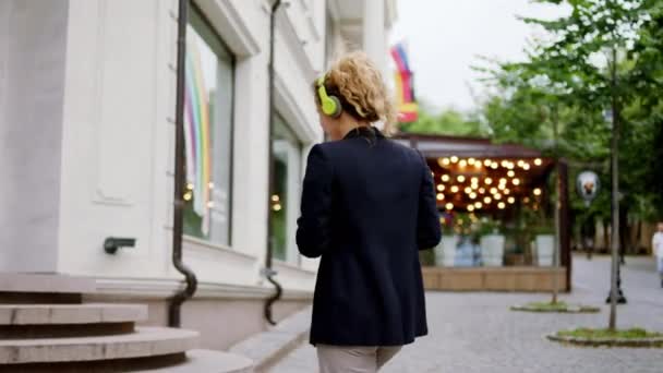 Moderní business street office pracovník žena chůze do moderní budovy držící digitální tablet a kávu a nošení sluchátek — Stock video
