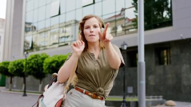 Dobře vypadající dáma před kamerou tančí a zpívá před kamerou uprostřed ulice poslouchá hudbu ze sluchátek — Stock video
