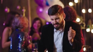 Genç adam kameranın önünde çok karizmatik bir şekilde dans ediyor ve elinde bir kadeh şampanya tutarak gecenin tadını çıkarıyor. Doğruca kameraya bakıyor.