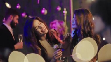 Doğum günü partisi gülümseyen iki çekici bayan partiden keyif alıyor ellerinde kokteyl kadehleriyle dans ediyorlar. ARRI Alexa Mini 'de çekilen