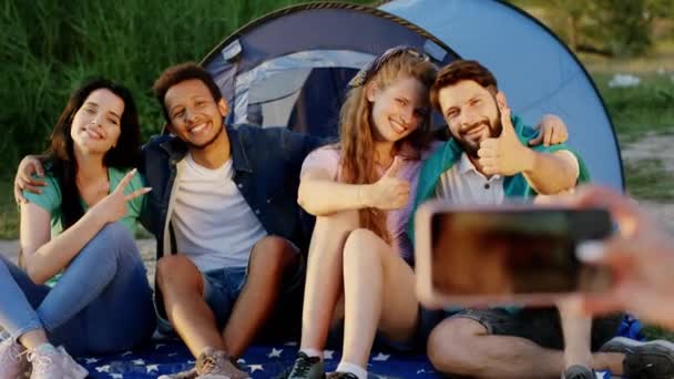 Buen grupo de amigos multirraciales posando en el picnic al lado de su tienda de campaña algún otro amigo tomar fotos con el teléfono. Disparo en ARRI Alexa — Vídeos de Stock