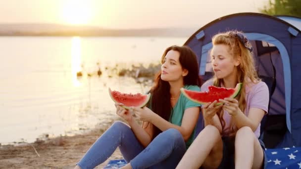 Niesamowity zachód słońca nad jeziorem dwie koleżanki panie jedzące smaczne kawałki arbuza i cieszące się czasem spędzonym na łonie natury — Wideo stockowe