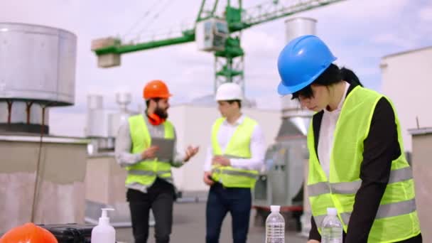 Stavební dělnice, inženýrka a architektka, se společně setkávají na střeše staveniště a analyzují plán stavby, které mají na sobě bezpečnostní přilby — Stock video