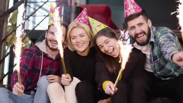 Dobrze wyglądający młodzi ludzie świętujący urodziny po tym jak skończyli studia w bibliotece używając iskry i mając urodzinowy kapelusz patrzą prosto w kamerę — Wideo stockowe