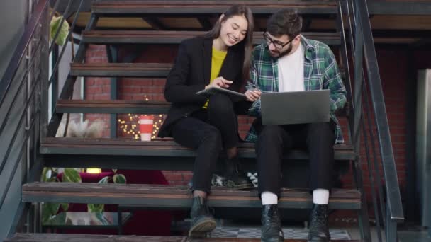 Carismática dama japonesa y su amigo de la universidad chico guapo con un vaso inteligente haciendo un proyecto juntos en la biblioteca después de la universidad — Vídeo de stock