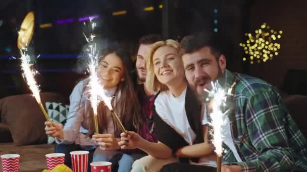 Impressionnant deux couples devant la caméra passer un bon moment ensemble célébrer un anniversaire ils prennent quelques étincelles tout en étant assis dans un salon moderne, ils apprécient le moment. 4k — Video