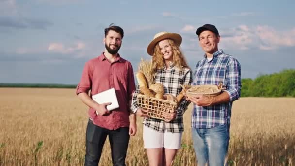 Bien parecido equipo de granjeros empresa familiar en el medio del campo de trigo de oro feliz dama con un sombrero sosteniendo un poco de pan fresco en una caja — Vídeos de Stock
