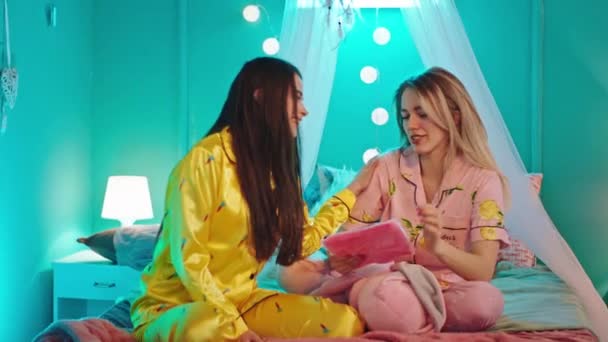 Karismatiska bästa vänner unga kvinnor chatta tillsammans medan de sitter på sängen i pyjamas de har en övernattning över tiden — Stockvideo