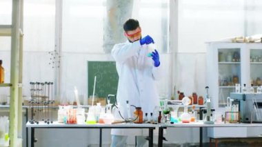 Biyoteknoloji laboratuarındaki bir adamda kimyasal reaksiyon deney yapmak için mavi bir sıvı kullanıyor ve koruyucu ekipman giydiği tepkiyi analiz ediyor.
