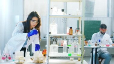 Biyoteknoloji laboratuvar ekibi bazı projeler üzerinde çalışıyor. Bazı kimyasal çözeltileri olan küvetler kullanıyorlar. Koruyucu ekipmanlar giyiyorlar. ARRI Alexa Mini 'de çekilen.