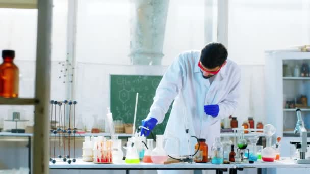 Forskare i det kemiska laboratoriet använder lite blå vätska på glaset för att göra en kemisk reaktion han bär skyddsutrustning. Skjuten på ARRI Alexa Mini. — Stockvideo