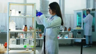 Bilim kadını ve asistanı biyoteknoloji laboratuarında birlikte çalışıyorlar. Cam küvette bazı kimyasal sıvılar kullanıyorlar. Sonuçları analiz ediyorlar.