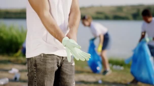 Zbliżenie do kamery szczegóły wolontariusza Weź rękawice ochronne zacząć nosić je przed rozpoczęciem czyszczenia śmieci z plaży — Wideo stockowe