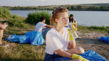 Plaj tarafında bir grup gönüllü için temizlik günü karizmatik sarışın bayan bir şişe su al ve arka planda büyük gölün önünde içmeye başla.