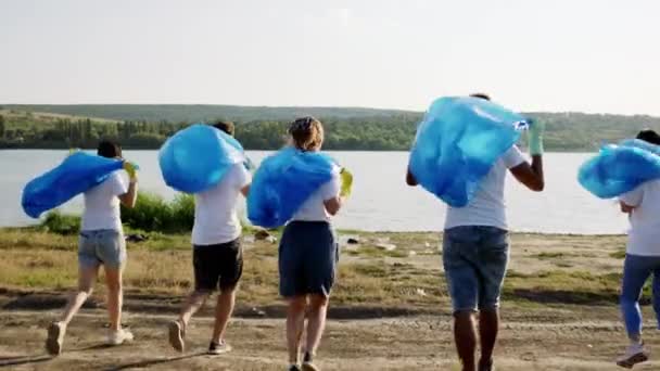 Gruppe freiwilliger Helfer am Strand neben dem See läuft zusammen und hält Plastiktüten, um den Müll einzusammeln — Stockvideo