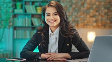 İş yerindeki sandalyede otururken doğrudan kameraya bakan gülümseyen güzel bir kadının portresi.