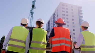 İnşaat alanında ustabaşı ve ekibinden oluşan çeşitli uzmanlar gelecek çalışmalarını inceliyor güvenlik kaskı ve gözlüğü takıyorlar.