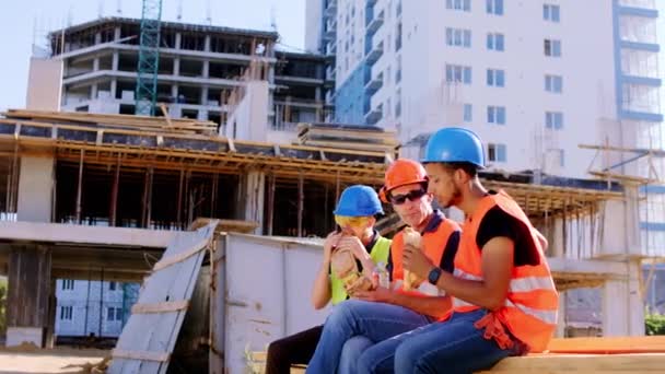 Tiempo de descanso en medio del sitio de construcción trabajadores multiétnicos y capataz tienen un tiempo de descanso se sientan y comienzan a comer algunos sándwiches — Vídeo de stock