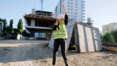 Beyaz kasklı, gözlüklü, kameranın önünde dans eden ve kulaklıklardan müzik dinleyen karizmatik genç mimar kadın.