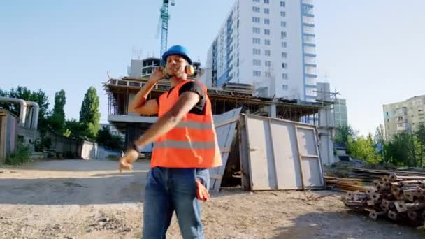 Caminando frente a la cámara chico afroamericano y empezar a bailar en el sitio de construcción a la hora del almuerzo al lado de sus colegas que todos llevan uniforme de protección — Vídeo de stock