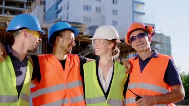 Усміхаючись великій багатоетнічній щасливій команді фахівців з будівництва, вони дивляться прямо на камеру і обіймають один одного позуючи. 4k — стокове відео