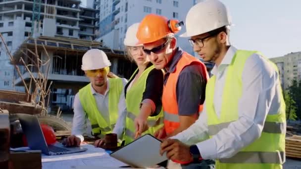 집중 된 다양 한 전문가들이 함께 건물 설계를 분석하고 안전 헬멧과 고글을 쓰고 있습니다. — 비디오